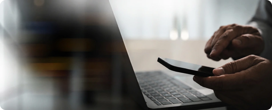 Person using a phone next to a laptop